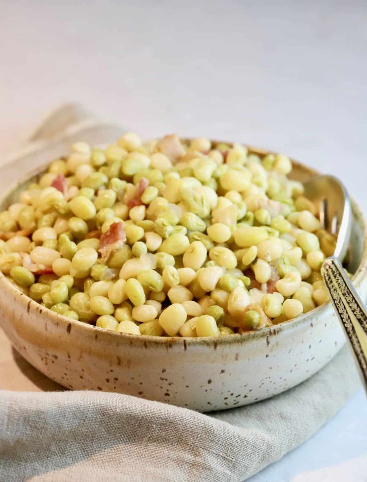 a white bowl filled with corn on top of a table next to a fork and napkin