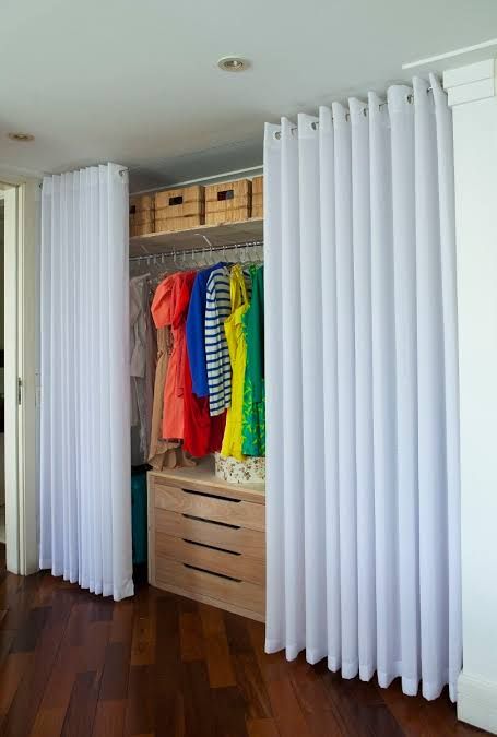 an open closet with white curtains and clothes