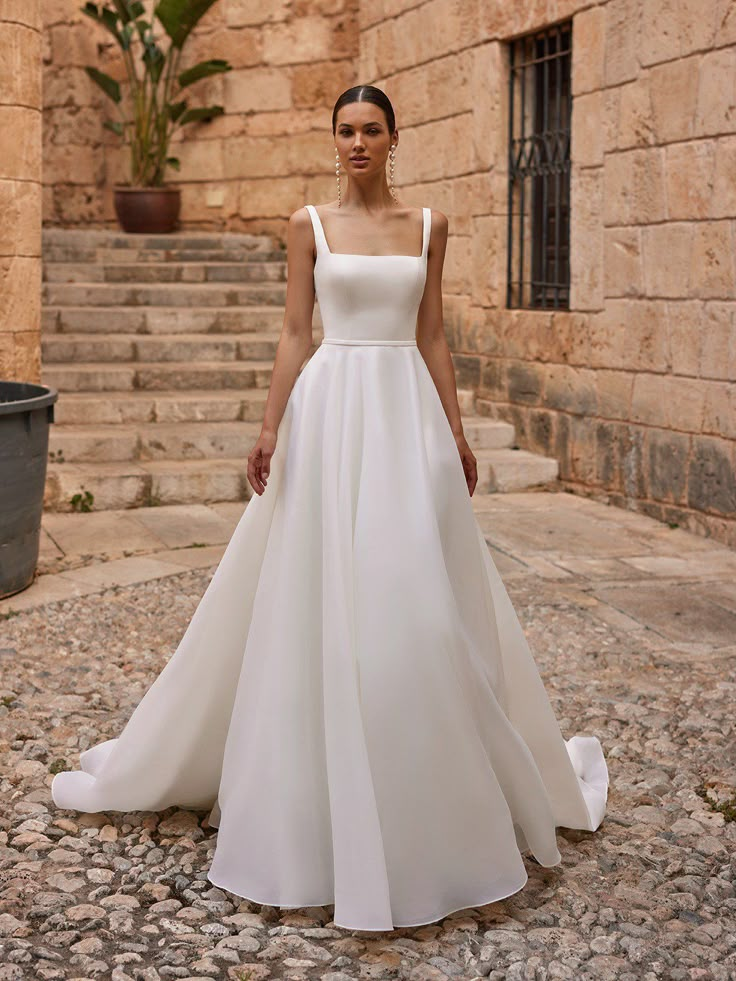 a woman in a white wedding dress standing on stone steps with her hands behind her back