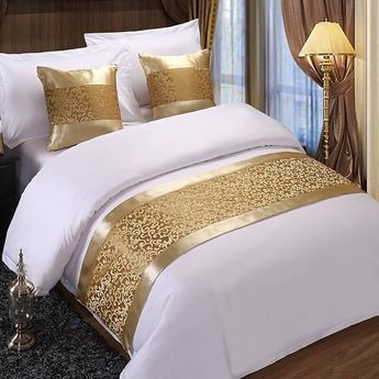 a bed with white and gold comforters in a bedroom next to a night stand