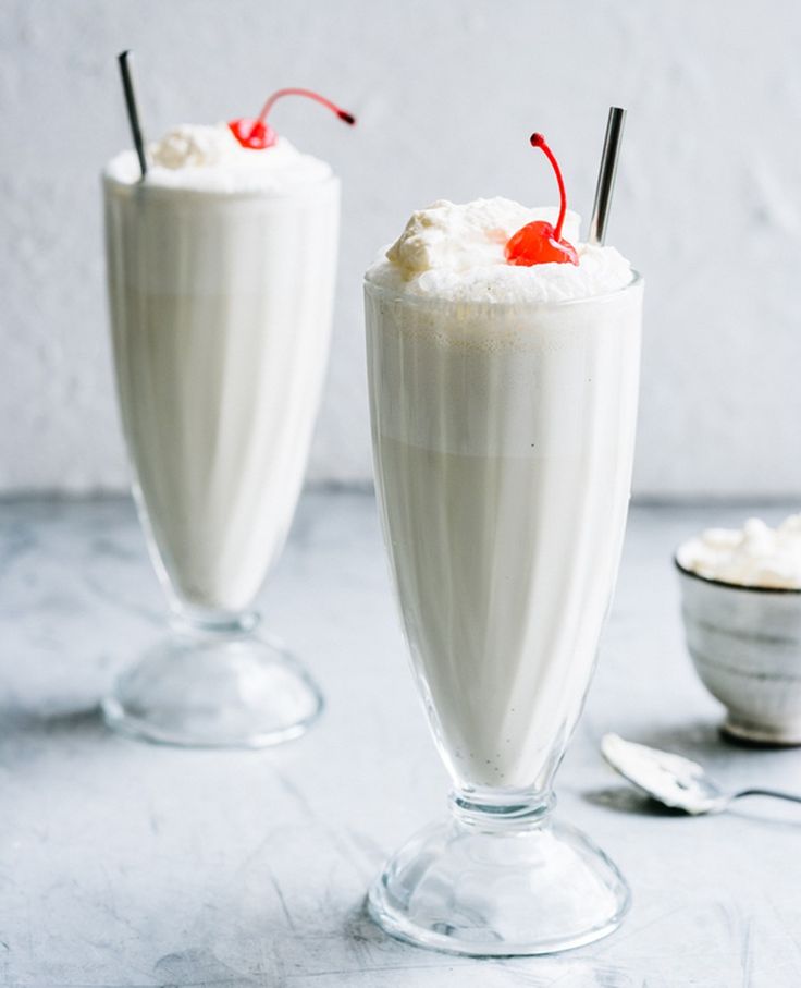 two glasses filled with ice cream and topped with whipped cream, cherry garnish