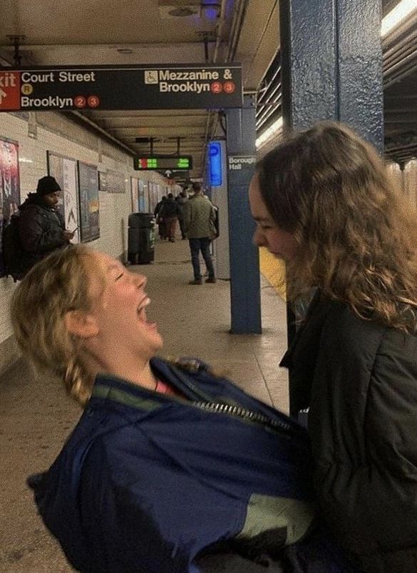 two women laugh as they sit on the subway platform