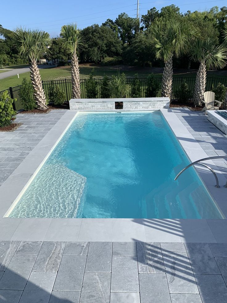 an empty swimming pool surrounded by palm trees and landscaping area with concrete pavers flooring