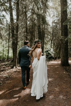 a bride and groom walking through the woods