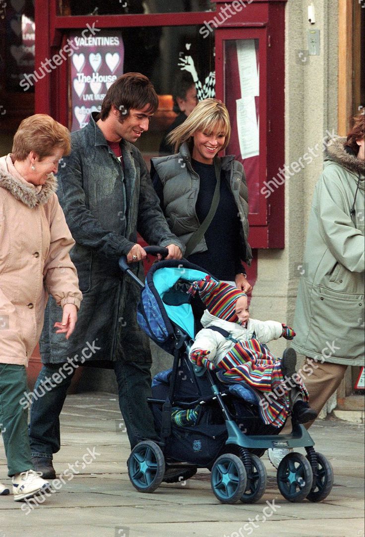 three people are walking with a baby in a stroller on the sidewalk, while two others