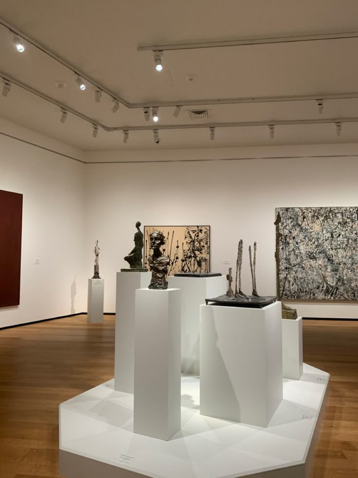 an art gallery with sculptures on pedestals and paintings on the wall in the background