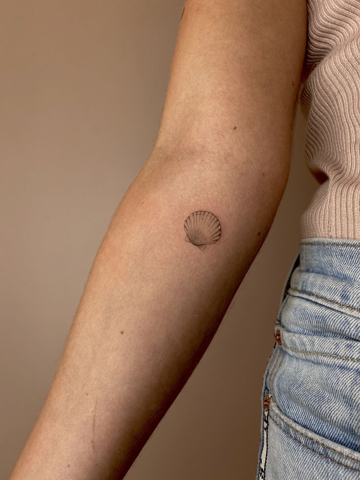 a woman's arm with a shell tattoo on the left side of her arm