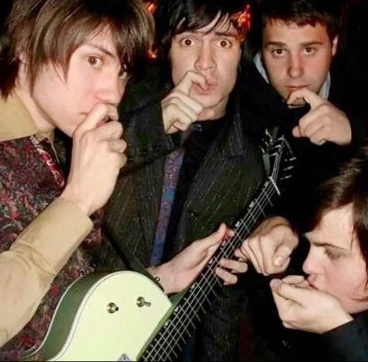 four young men are posing for the camera while one man is holding an electric guitar