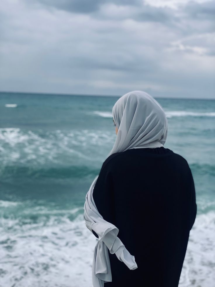 a woman standing on top of a beach next to the ocean under a cloudy sky