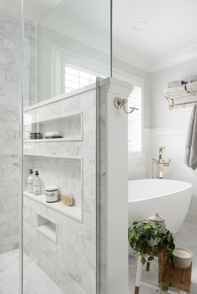 a white bathroom with marble walls and flooring, along with a walk in shower