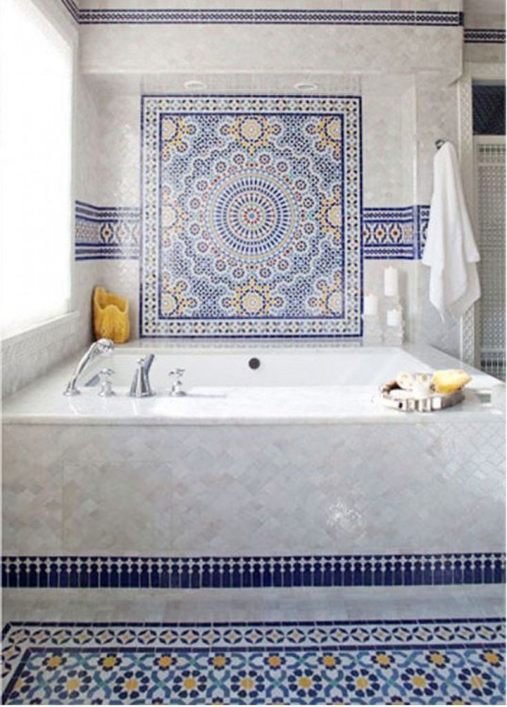 a bath tub sitting next to a window in a tiled bathroom with blue and yellow accents