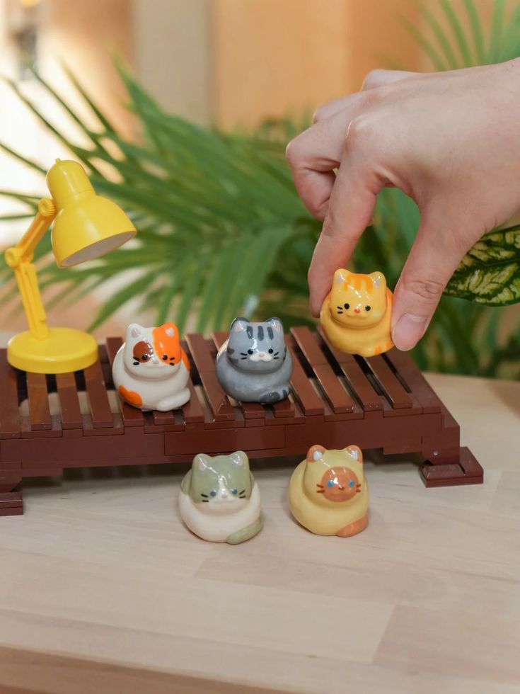 a hand reaching for small toy animals on a wooden table next to a potted plant