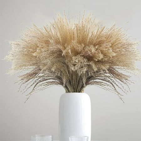 a white vase filled with dry grass on top of a table next to two glasses