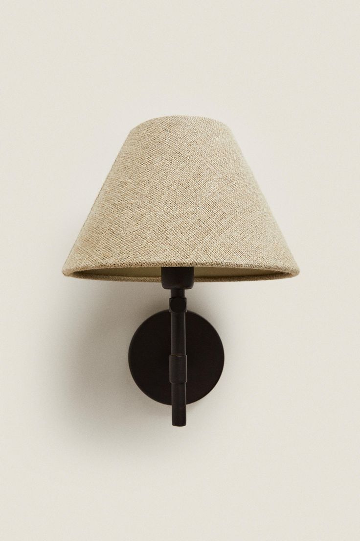 a wall mounted light with a beige shade on it's face and black base