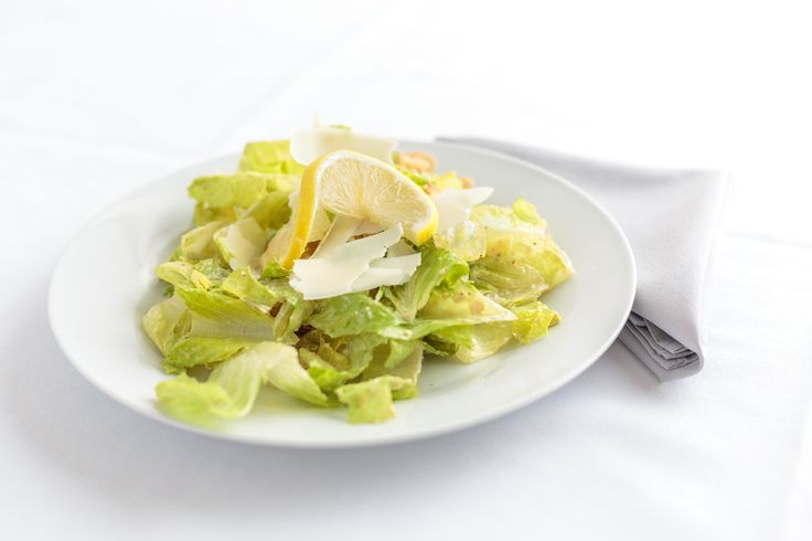 a white plate topped with a salad covered in lettuce and lemon wedges