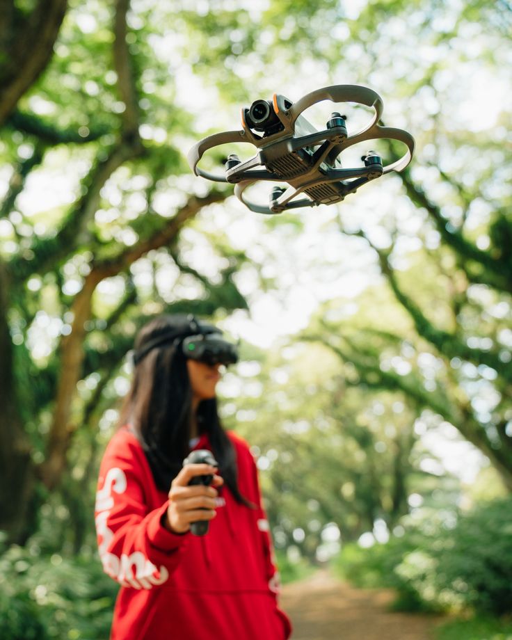 a woman standing in the woods looking at her cell phone and flying a quadcopte