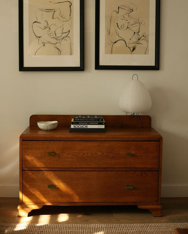 two framed pictures hang on the wall above a dresser