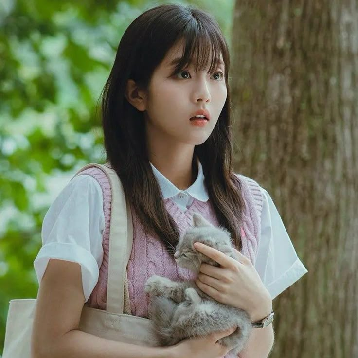 a woman holding a cat in her arms while standing next to a tree and looking at the camera