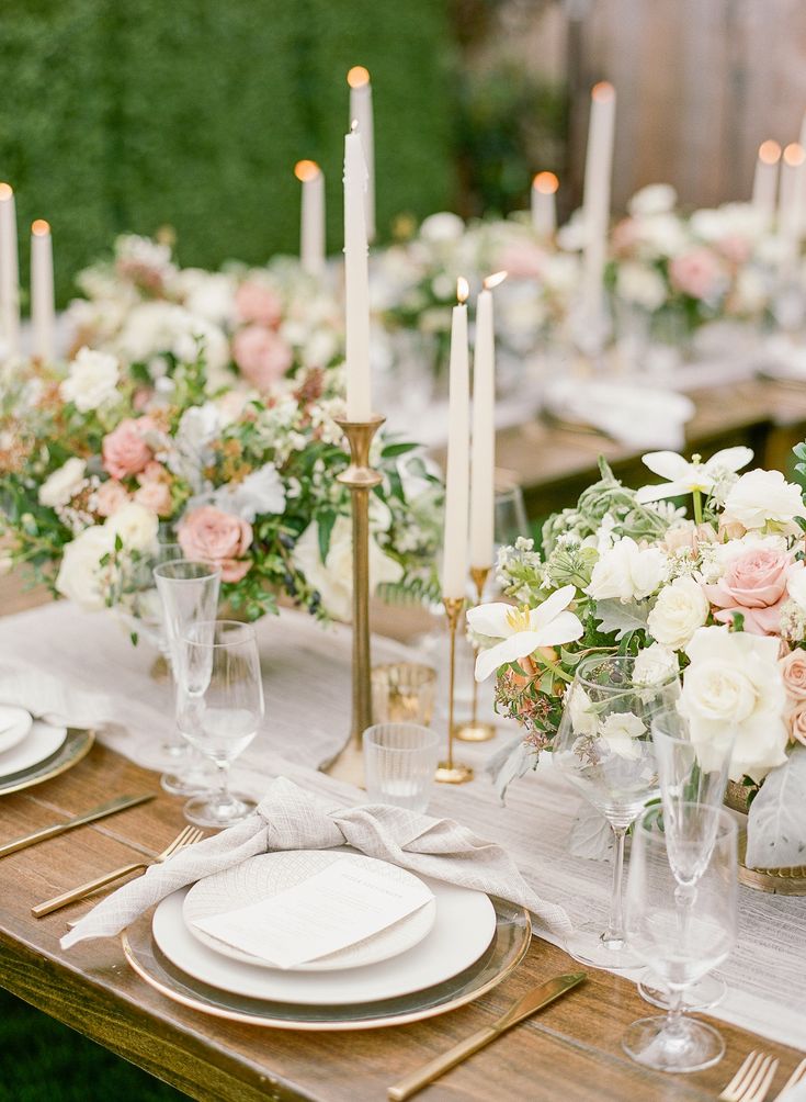 the table is set with white and pink flowers, gold candlesticks, and glassware