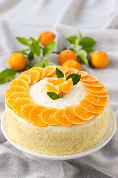 a cake with orange slices on it sitting on a white plate next to some green leaves