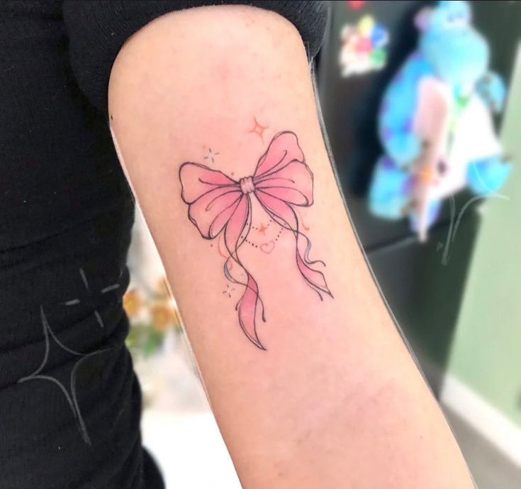 a woman's arm with a pink bow tattoo on the left side of her arm