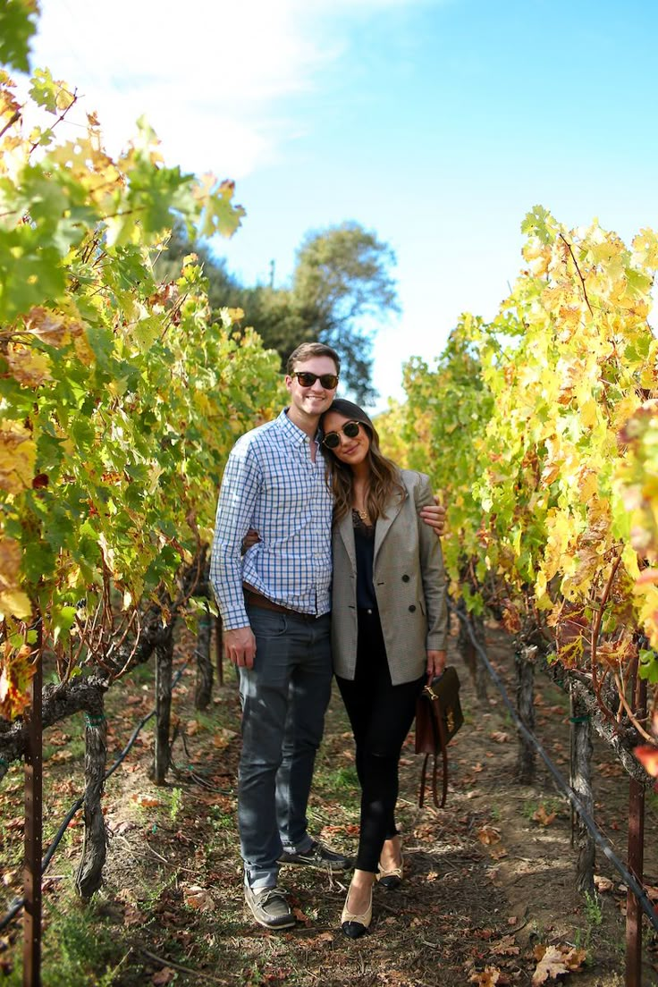 a man and woman standing next to each other in the middle of rows of vines