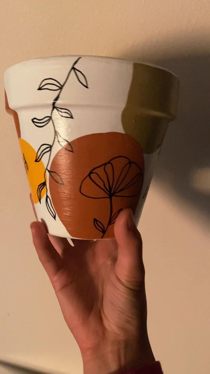 a hand holding up a paper cup with leaves painted on the outside and inside it