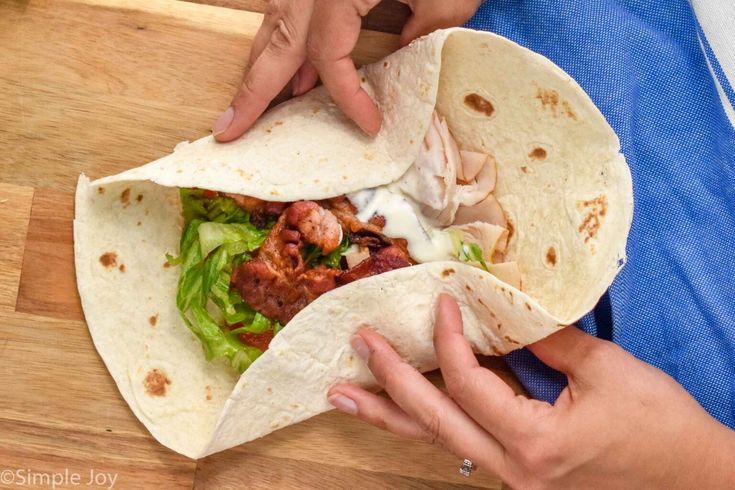 a person holding a tortilla with meat and lettuce