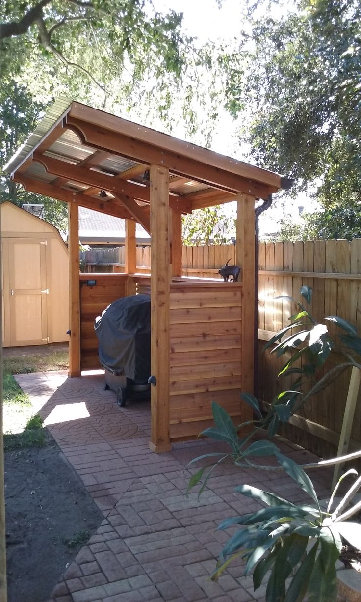 a wooden gazebo in the middle of a yard with a bbq and grill