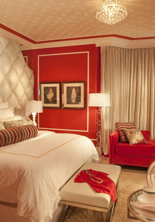 a bedroom decorated in red and white with a bed, chair, ottomans, lamps and pictures on the wall