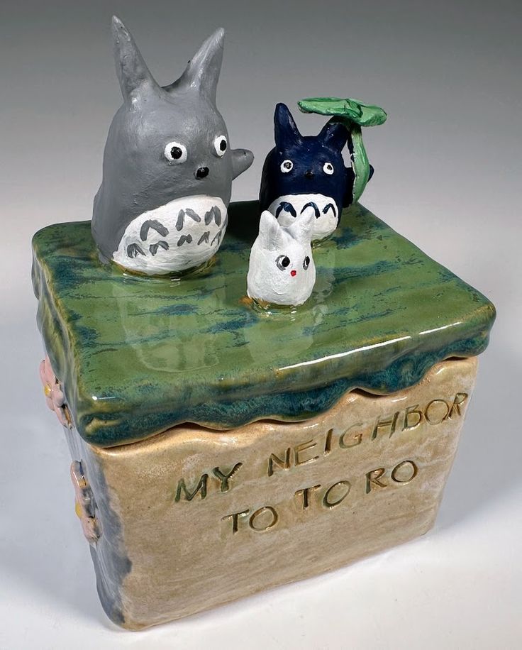 two ceramic figurines sitting on top of a book with the words my neighbor totoro