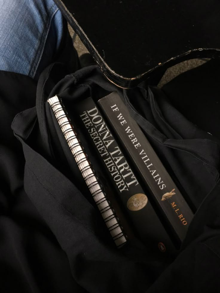 three books sitting on top of a black book bag next to a pair of jeans