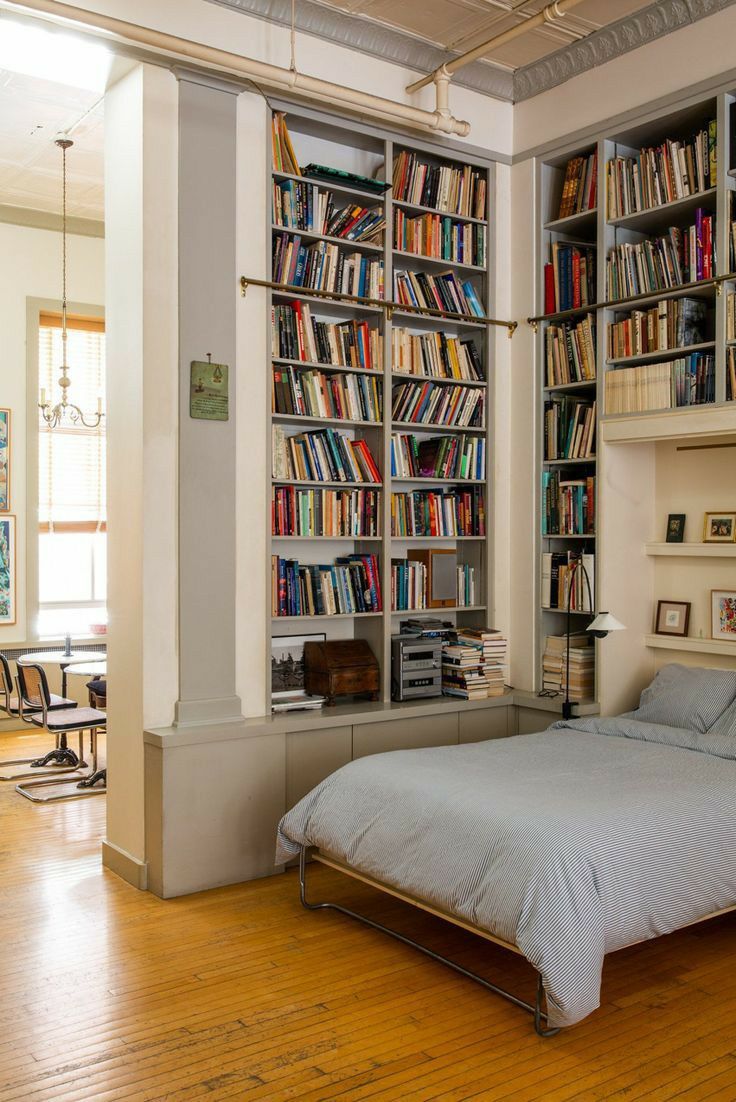 a bed sitting in front of a book shelf filled with books on top of a hard wood floor