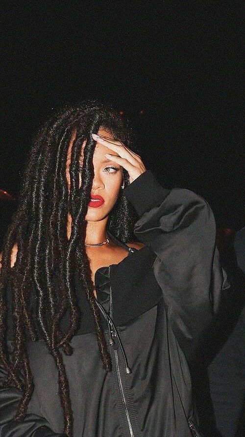 a woman with long dreadlocks is holding her hand up to her face and looking at the camera