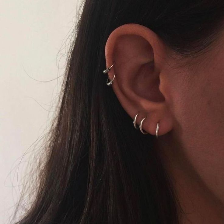 a woman's ear with three small silver rings on it