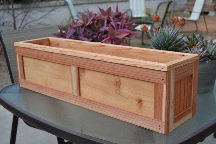 a wooden planter box sitting on top of a metal table next to some plants