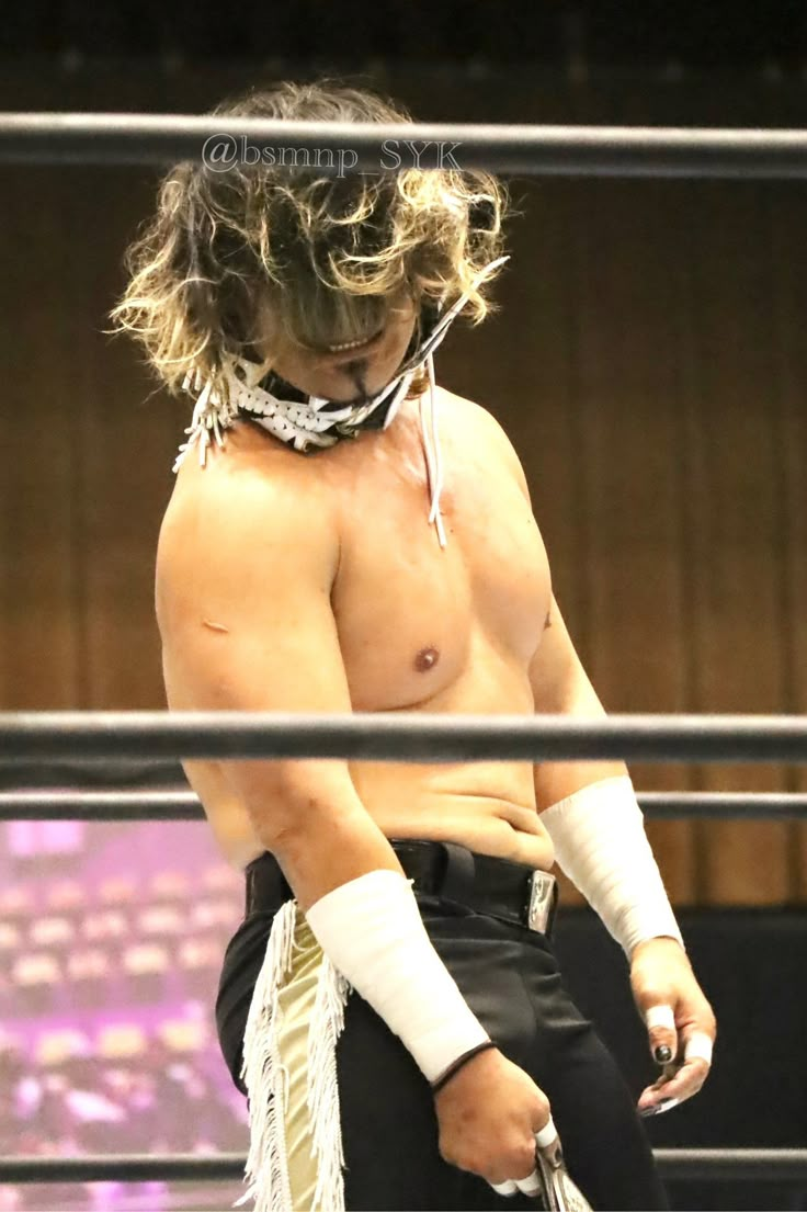 a shirtless man with no shirt on standing in a wrestling ring holding a rope