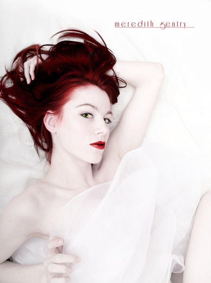 a woman with red hair laying on top of a white bed next to a pillow