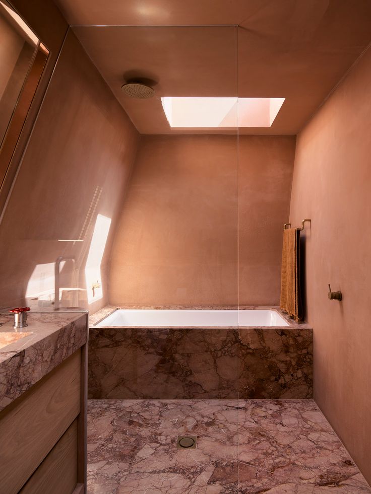 a bath room with a sink a mirror and a bath tub under a skylight