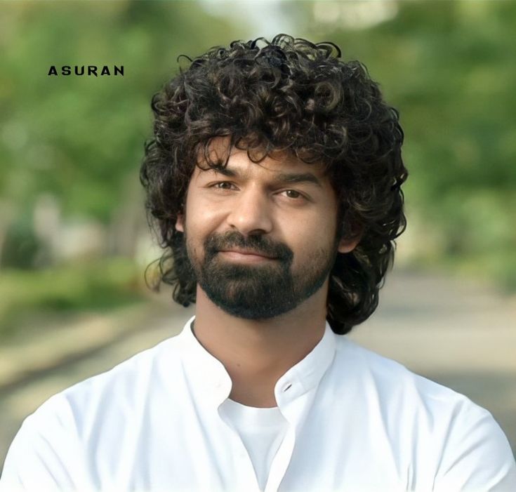 a man with curly hair and beard wearing a white shirt is looking at the camera