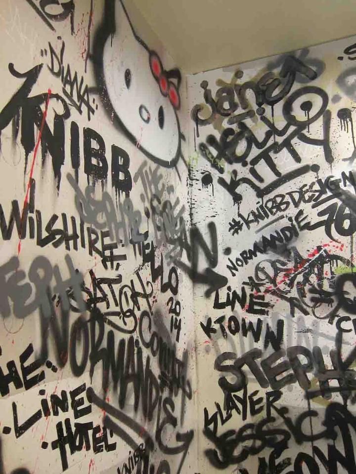 graffiti is on the wall next to a toilet in a public restroom with walls covered in black and white writing