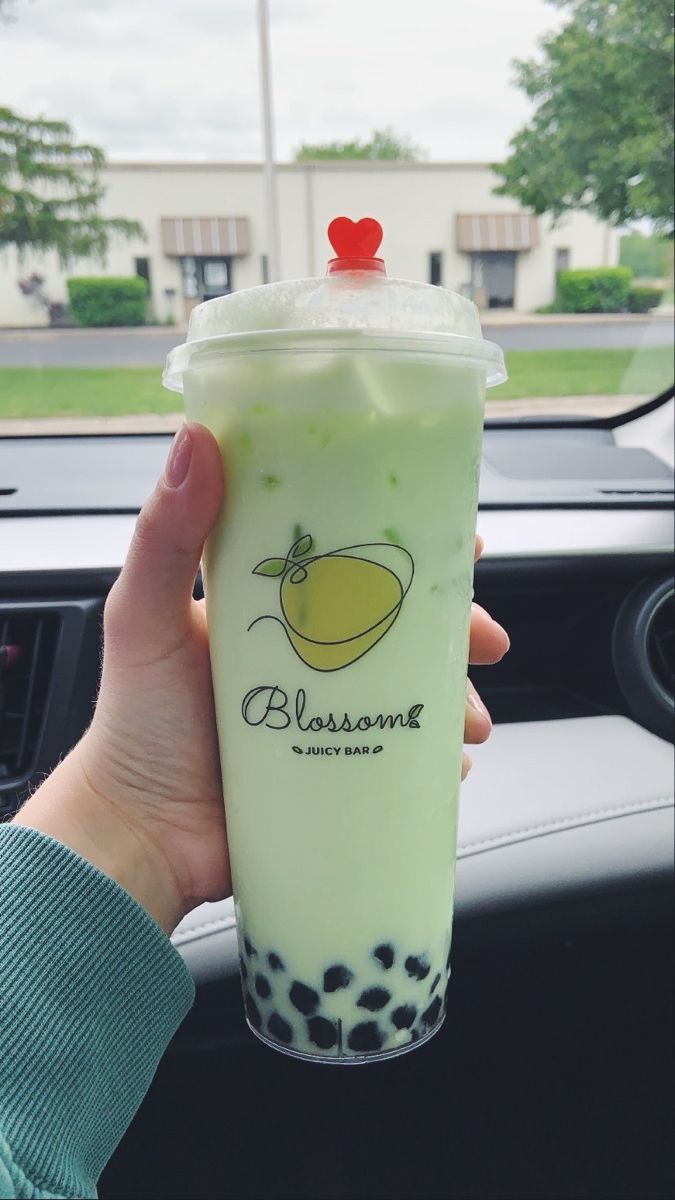 a person holding up a drink in their hand while sitting in a car with the steering wheel behind them