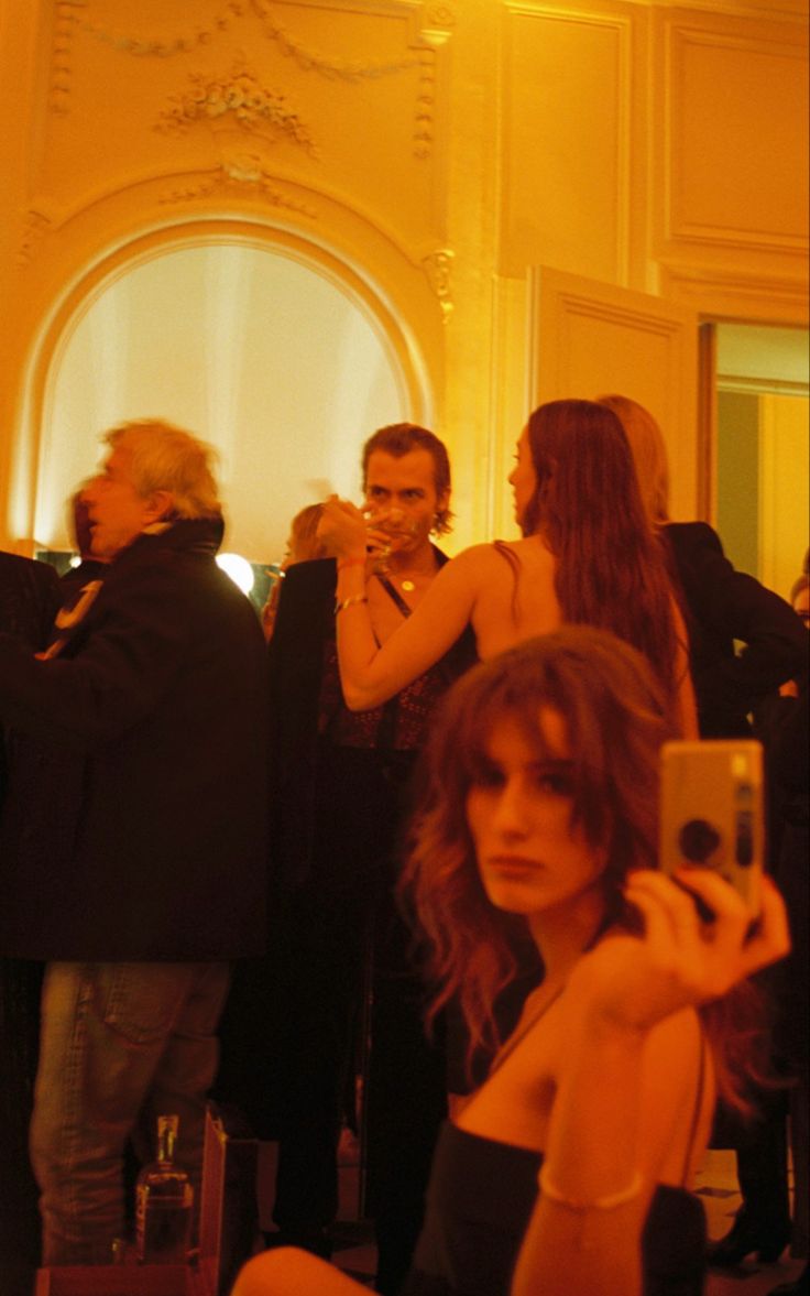 a woman taking a selfie with her cell phone in a room full of people