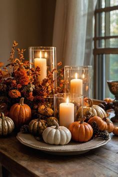 a table topped with candles and pumpkins on top of a wooden table next to a window