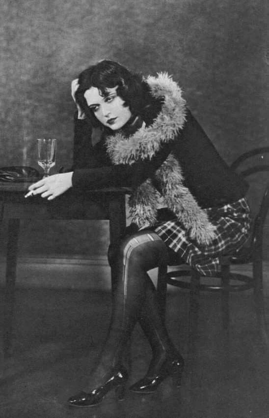 an old photo of a woman sitting at a table with a wine glass in her hand