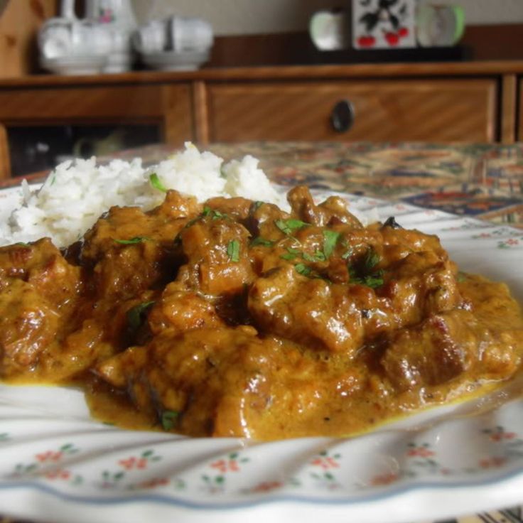 a white plate topped with meat covered in gravy next to rice on a table