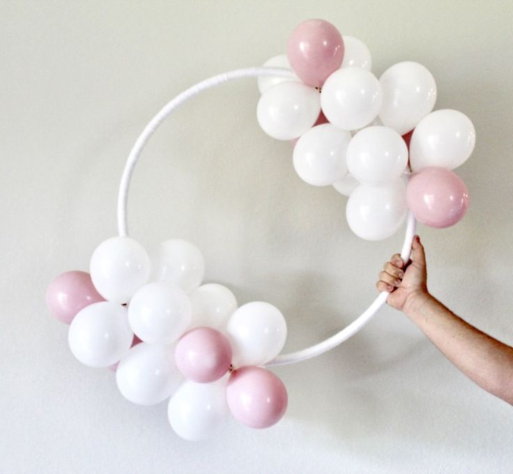 a person holding balloons in front of a white circle with pink and white balls on it