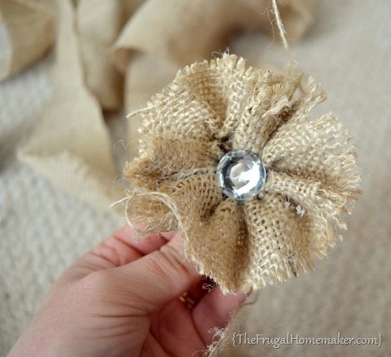 someone is holding a burlap flower with a bead in it's center