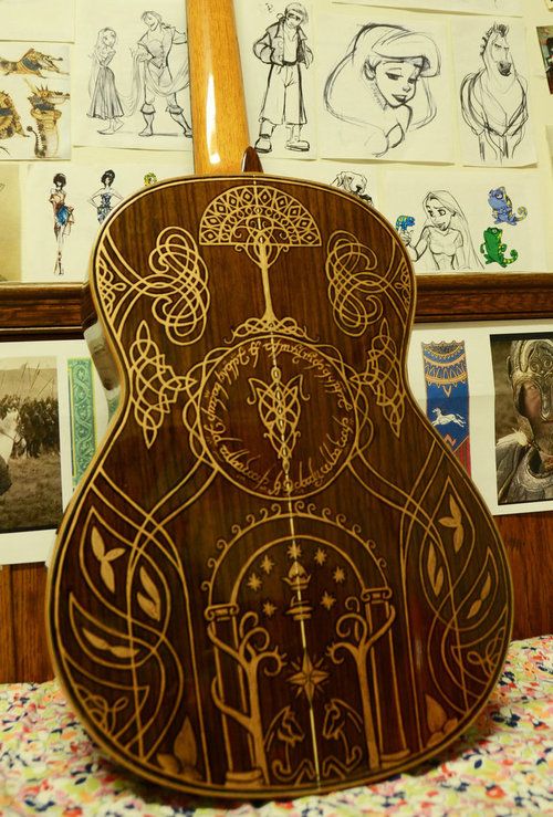 a wooden guitar sitting on top of a table next to pictures and drawings hanging on the wall