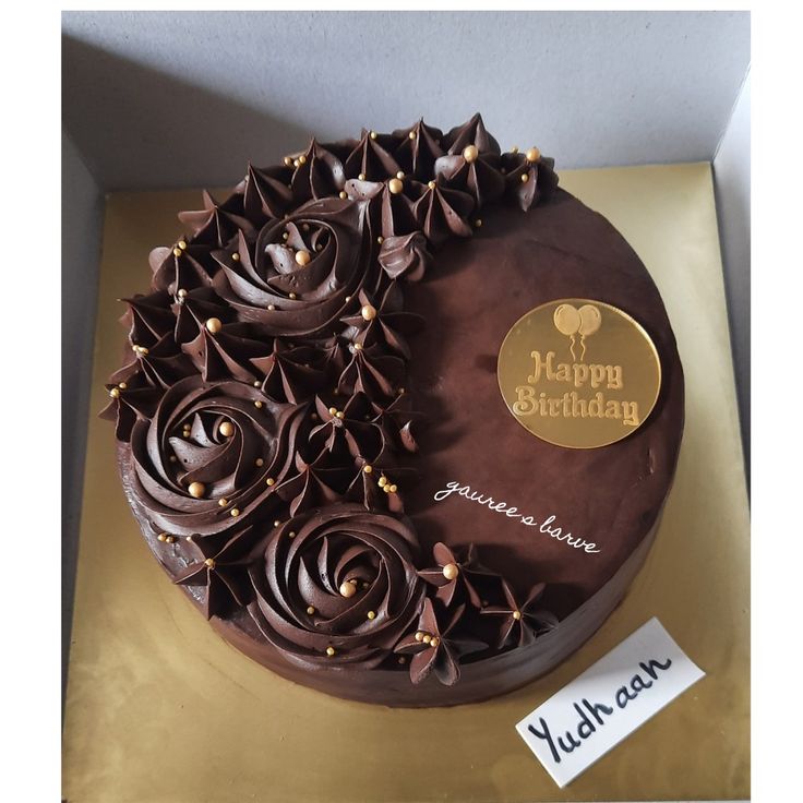 a birthday cake with chocolate frosting and decorations on it's side, sitting in a box